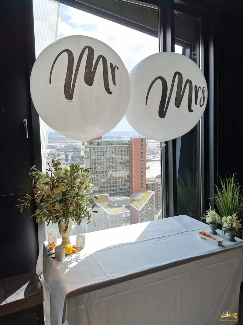 Weiße Mr.- und Mrs.-Ballons vor einem Fenster mit Hafenblick
