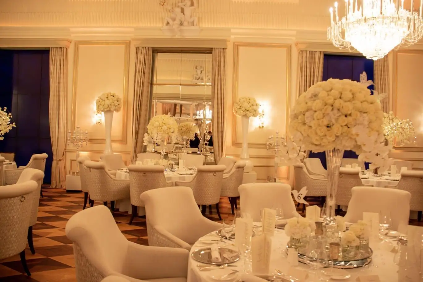 Festlicher Saal mit weißen Blumengestecken und gedeckten runden Tischen